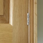 A close-up of an in-frame kitchen cabinet showing the exposed butt hinge