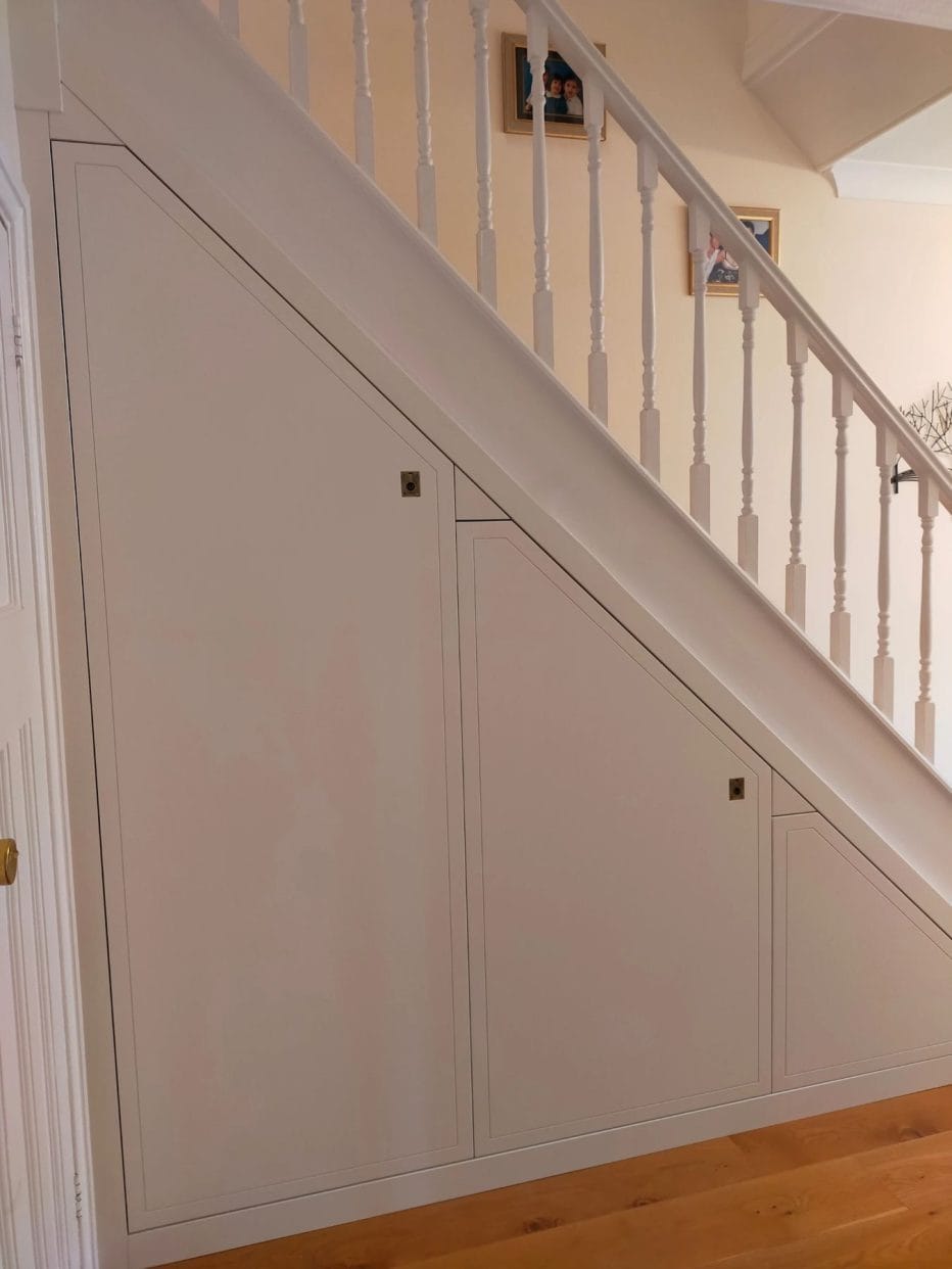 Side view of a stair case featuring white wooden balustrade and three smart under stair doors each featuring a flush brass ring pull. 