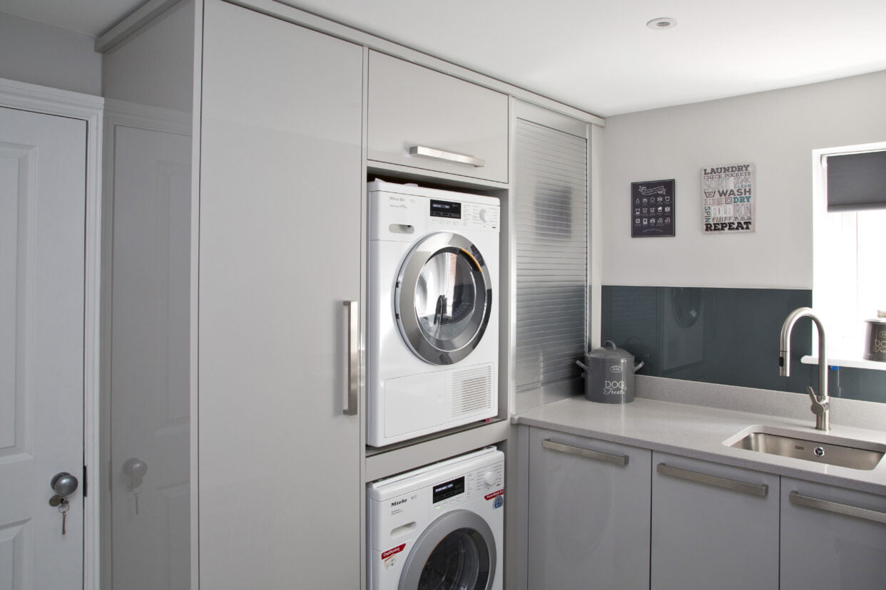 Utility room with stacked Miele appliances and tall corner cupboard