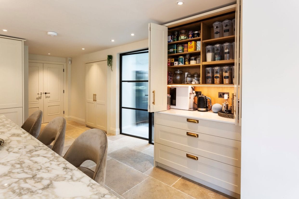 Cream shaker kitchen with brass accents. Open doors demonstrate a well-organised pantry cupboard.