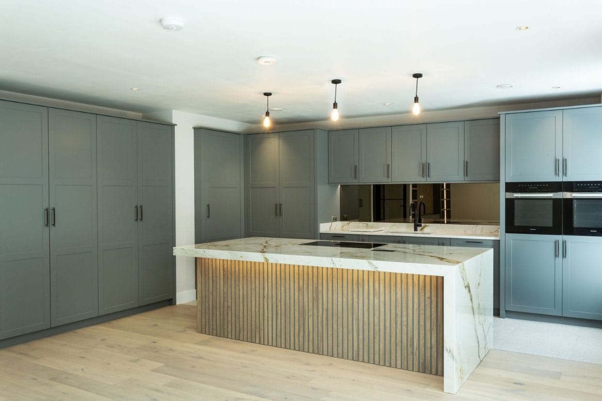 Grey shaker kitchen with wooden floor, featuring an elegant central island with marble countertop and slatted wood base.