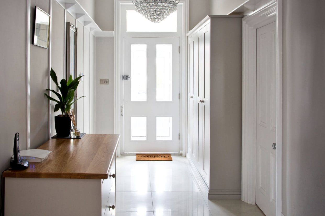 A bright, minimalist hallway with tiled floor and ample, full height cupboards.