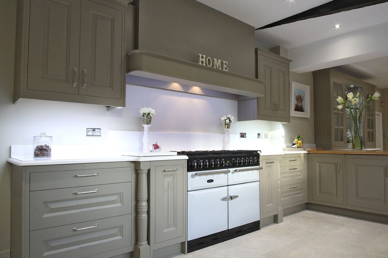 Elegant sage shaker kitchen with a range cooker and a sign above it that reads ‘Home’, there is a vase of amaryllis on the counter.