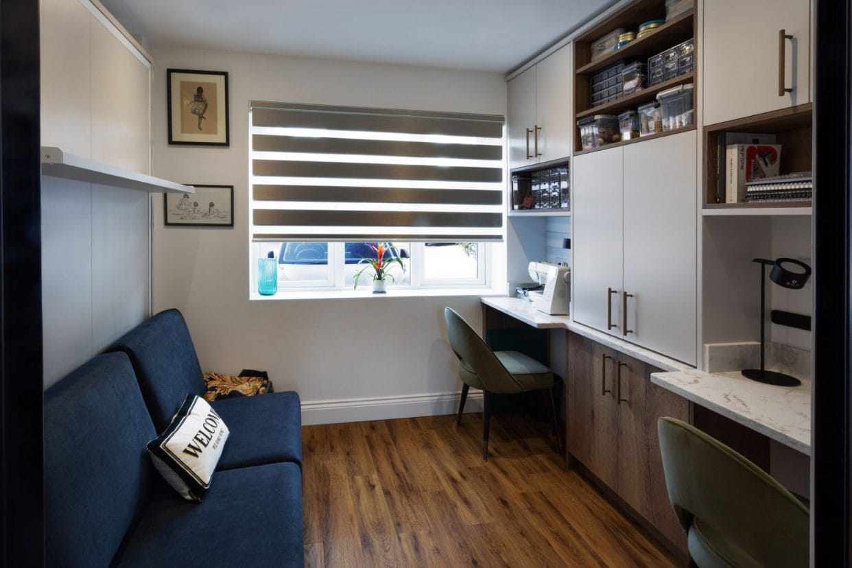 Craft room with sofa opposite twin desks and neatly organised craft supplies.
