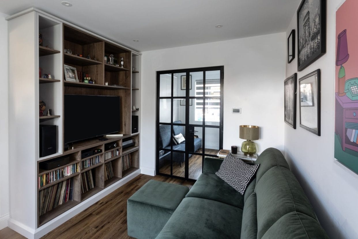 Media room with sofa and footstool opposite a wall of bespoke cabinetry for TV and music collection.