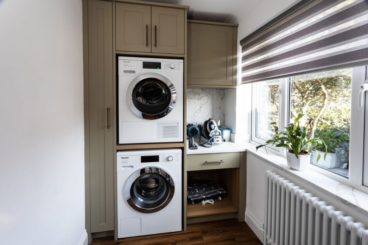 Stacked washer and dryer appliances within smart shaker-style cabinetry finished in a deep sage green – every part of the space has been used for storage.