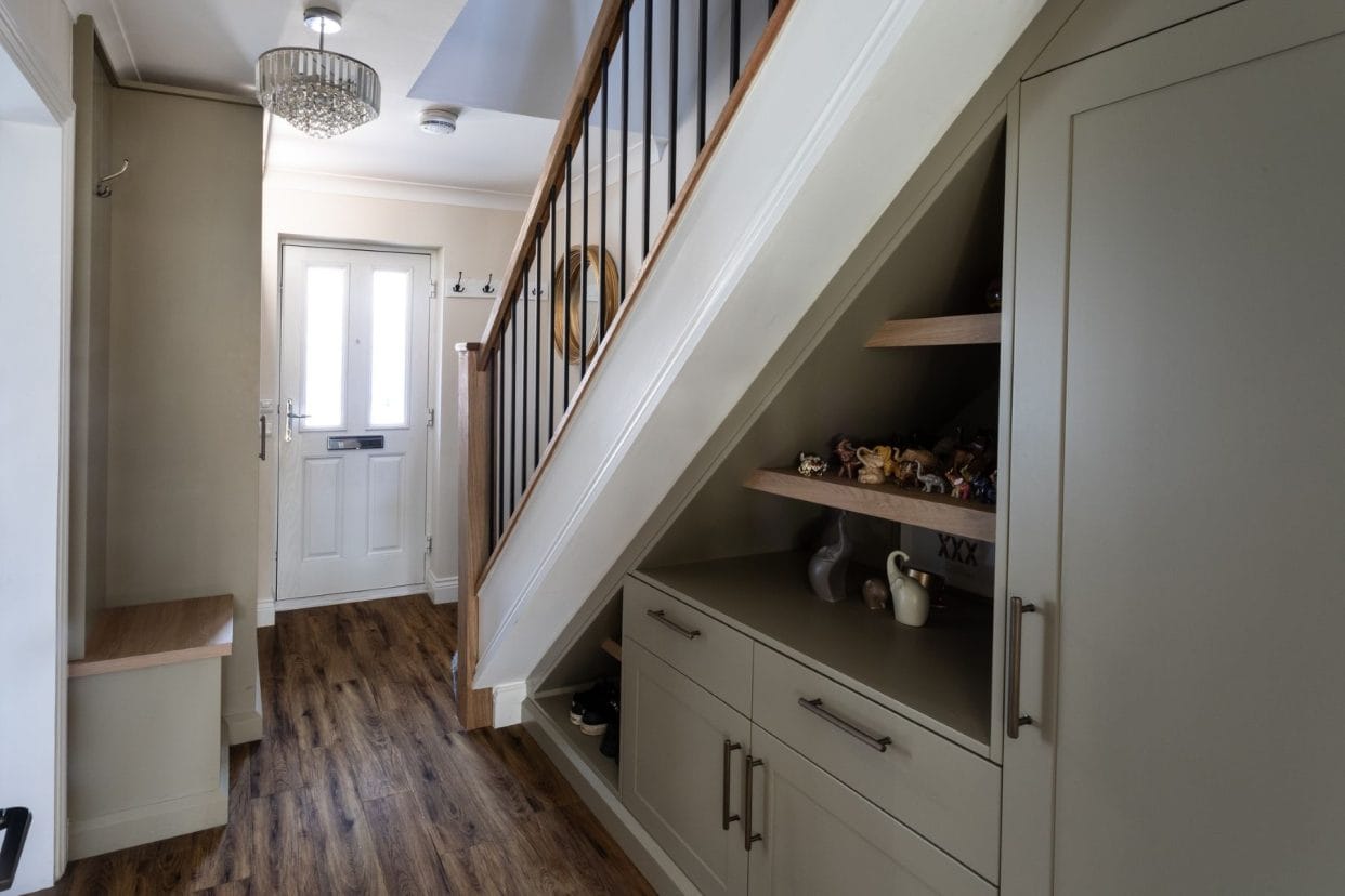 View of the under stairs towards the front door showing neat under stair storage in the deep sage green, with display shelving for ornaments as well as drawers and cupboards.