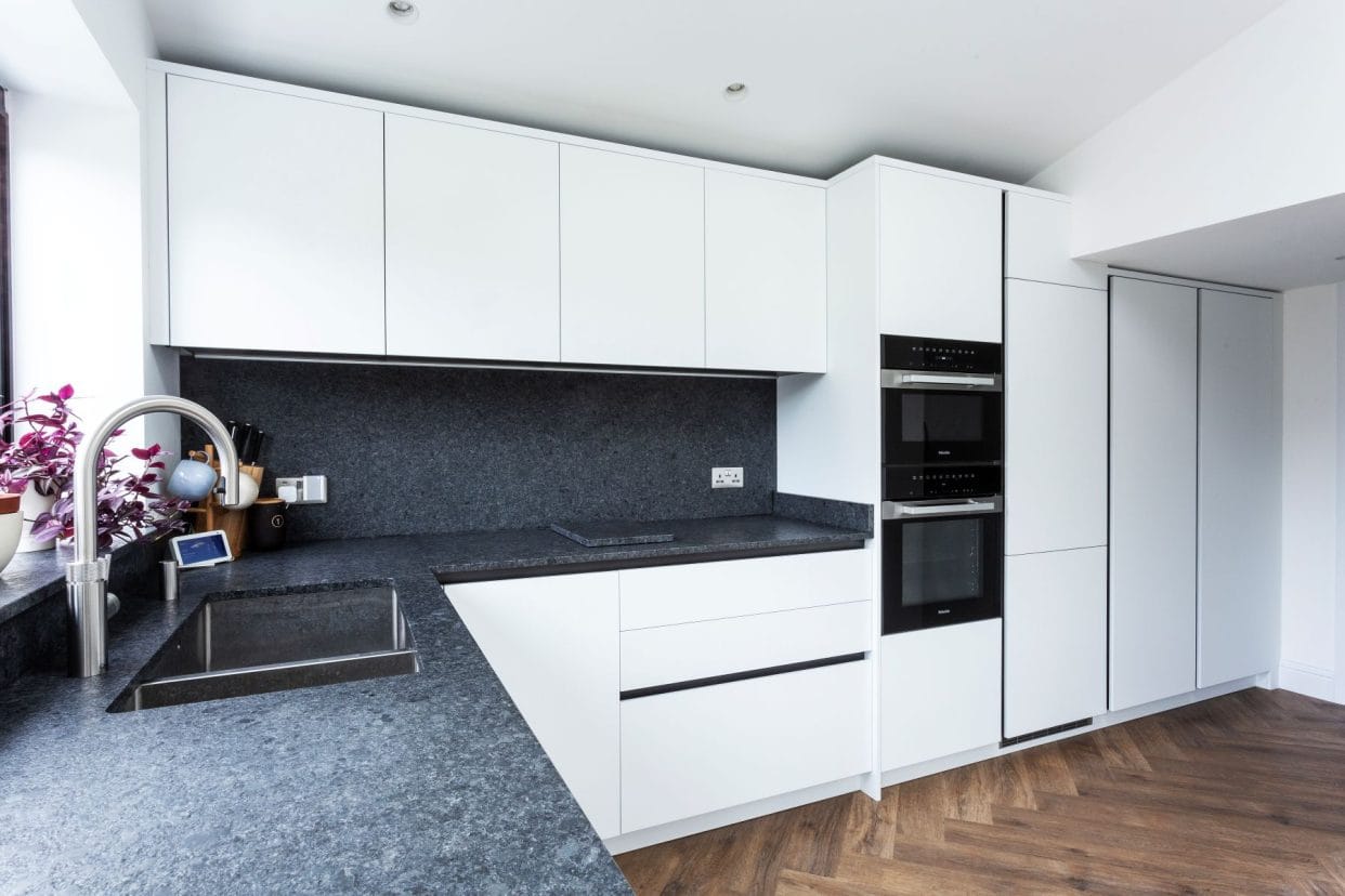 A modern kitchen with simple, gloss white flat panel doors, wood parquet flooring and grey granite countertops. 