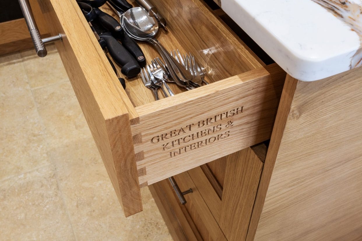 Close-up of an open drawer showing expert craftmanship in the dovetail joints and the inscription: Great British Kitchens & Interiors to the side of the drawer box.