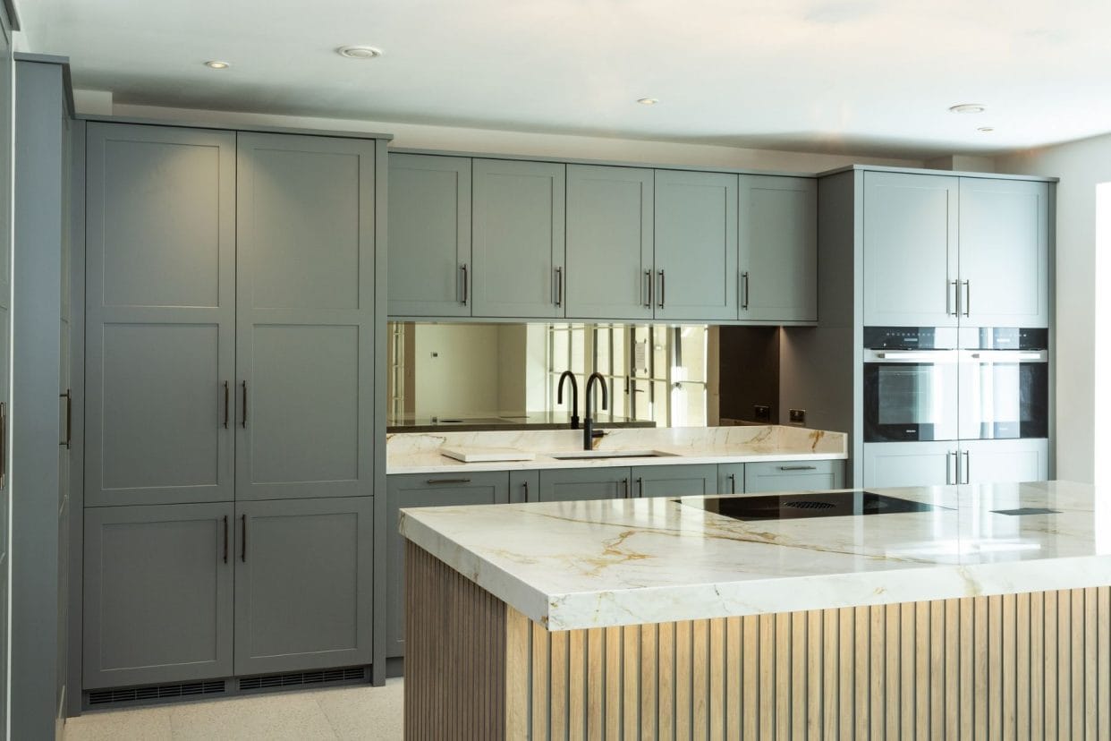 An elegant kitchen with full-height grey shaker cabinetry, marbled countertops, a mirrored splashback and slatted island panelling.