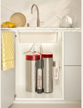 An open under-sink cupboard showing the Quooker hot water and CUBE tank sitting neatly alongside each other.