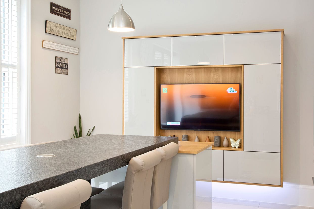 A wall-mounted media unit featuring a central screen surrounded by translucent glass cabinetry doors with oak beading.