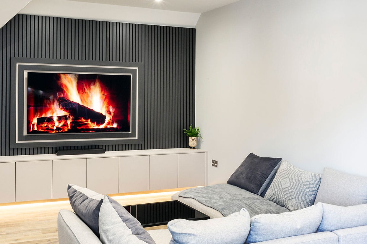 A contemporary media unit featuring a large screen mounted against dark grey slatted panelling. A sofa with plenty of cushions faces the screen.