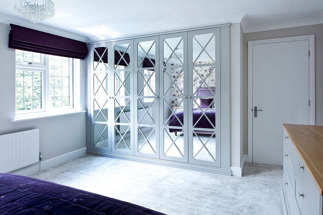 A light bedroom with a mirrored wardrobe featuring a geometric lattice design in white.