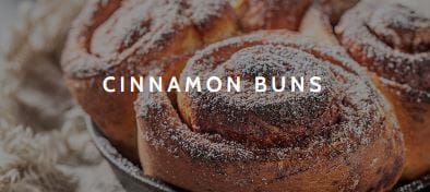 A close-up or three cinnamon buns dusted with icing sugar.