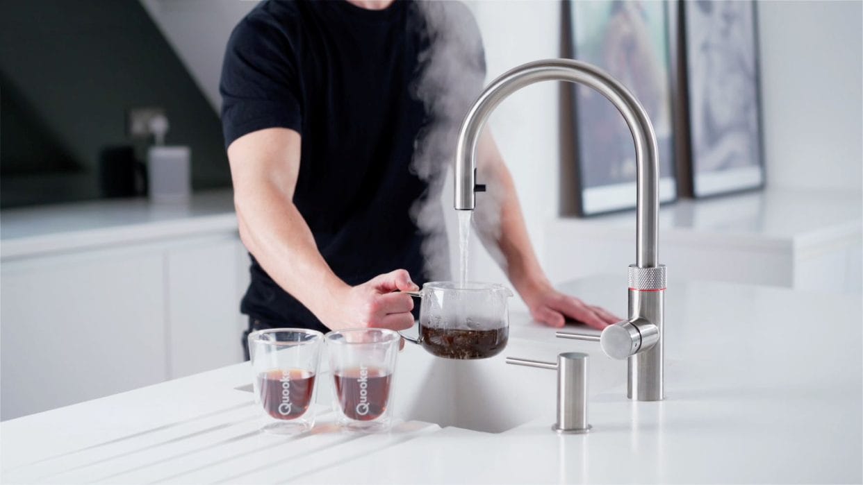 Image of a man in a black t-shirt demonstrating the Quooker instant boiling water tap by filling a glass teapot.