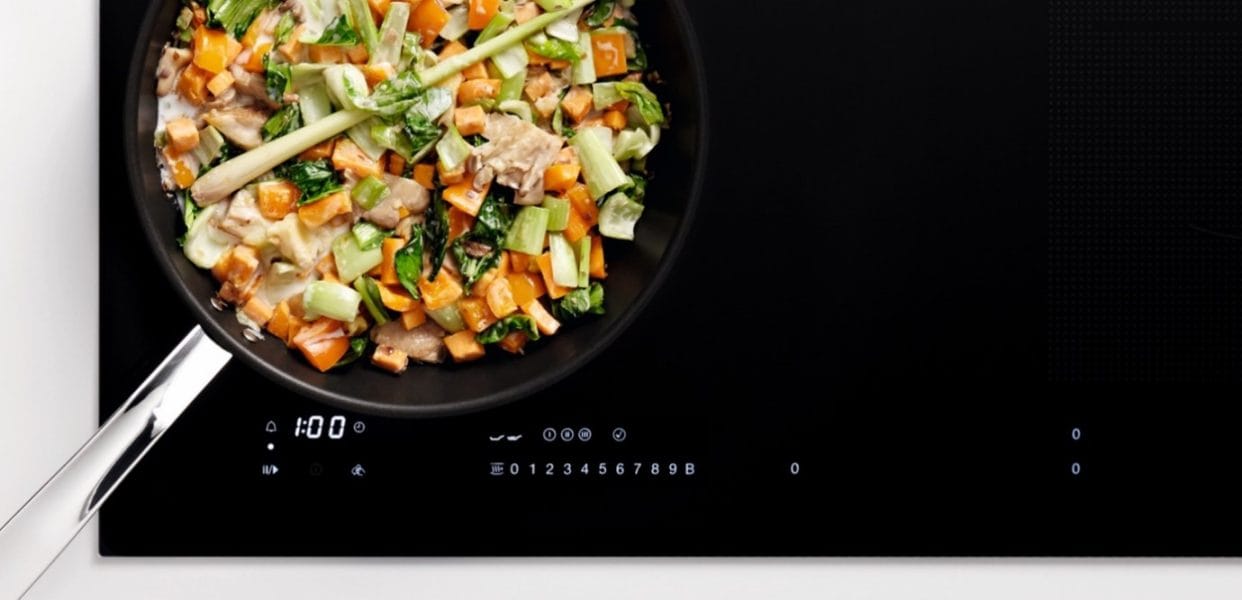 The sleek Miele induction hob with a stir fry pan of healthy chicken and vegetables.