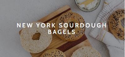 Freshly cut bagels on a wooden board and white cotton tea towel.