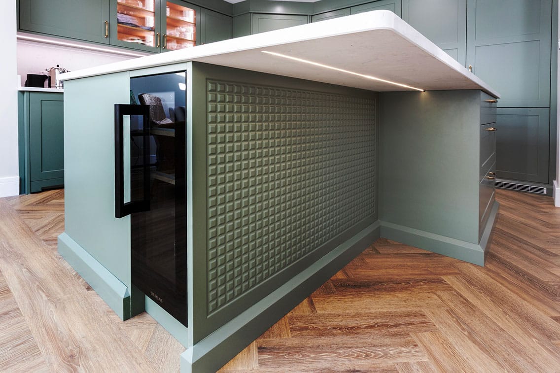 View from the underside of a stylish kitchen island demonstrating bespoke feature panelling and built-in wine fridge.