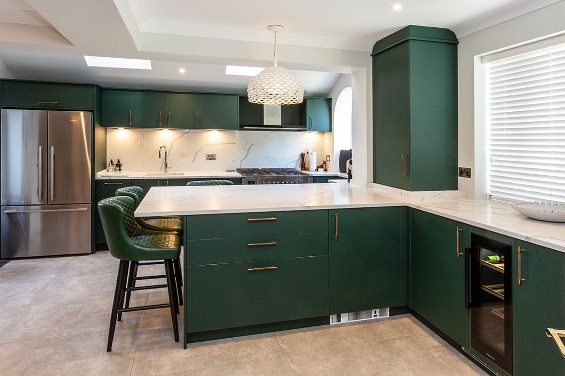 An elegant kitchen with flat panel cabinetry doors in a rich forest green, finished with brass bar handles.