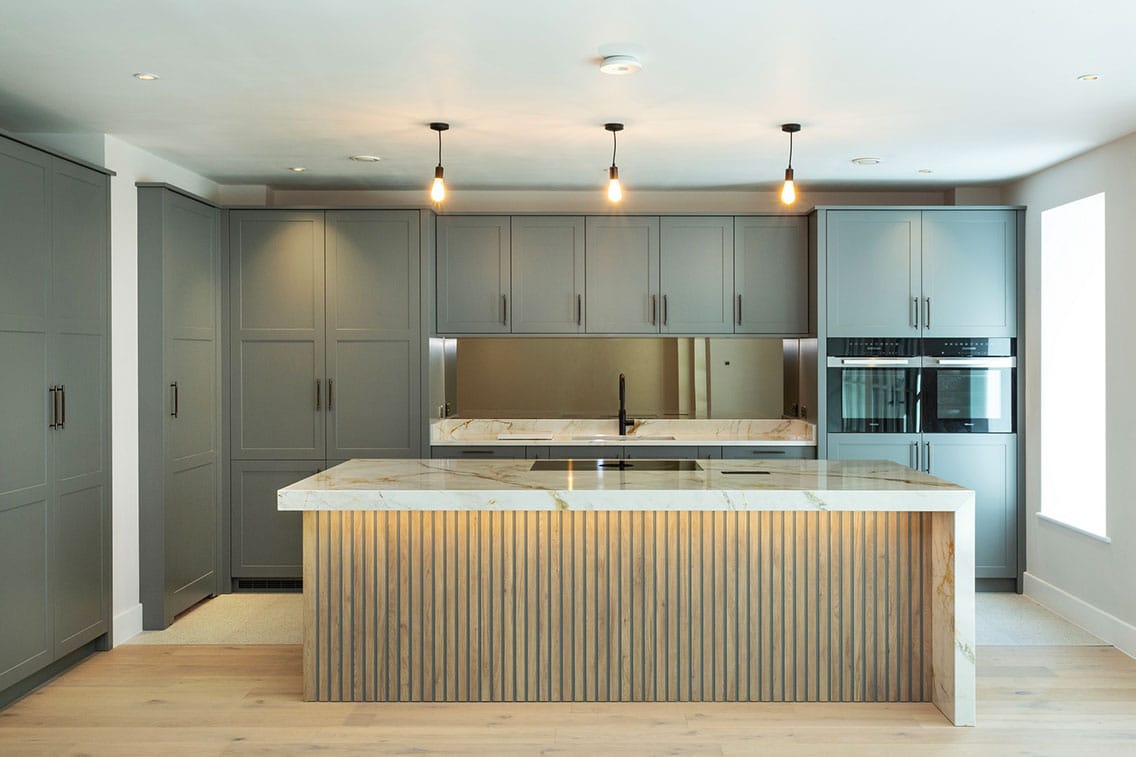 A beautiful bespoke shaker kitchen in a dove grey-painted finish with a statement kitchen island featuring a marble waterfall edge and bespoke panelling.