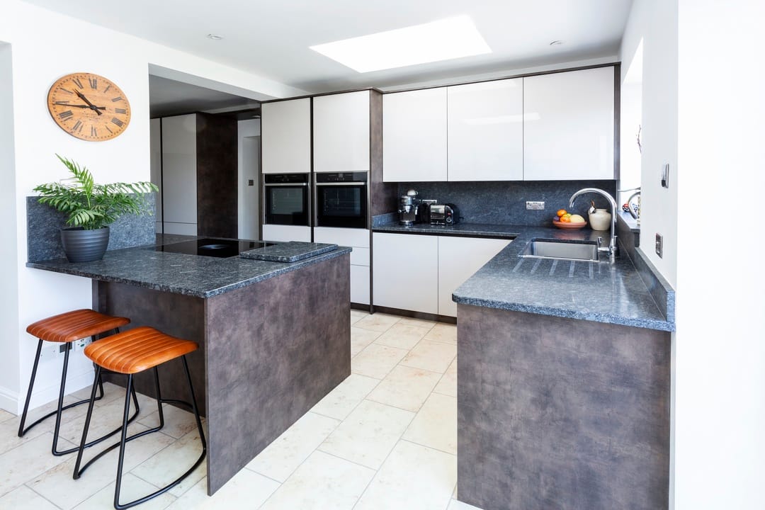A modern L-shaped kitchen with white flat panel cabinetry contrasting with rich grey granite worktops. There is space for an island breakfast bar.