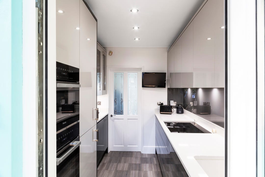 A small galley kitchen in a sleek black and white design with a mixture of split level and full height handmade cabinetry, with a door to the far end.