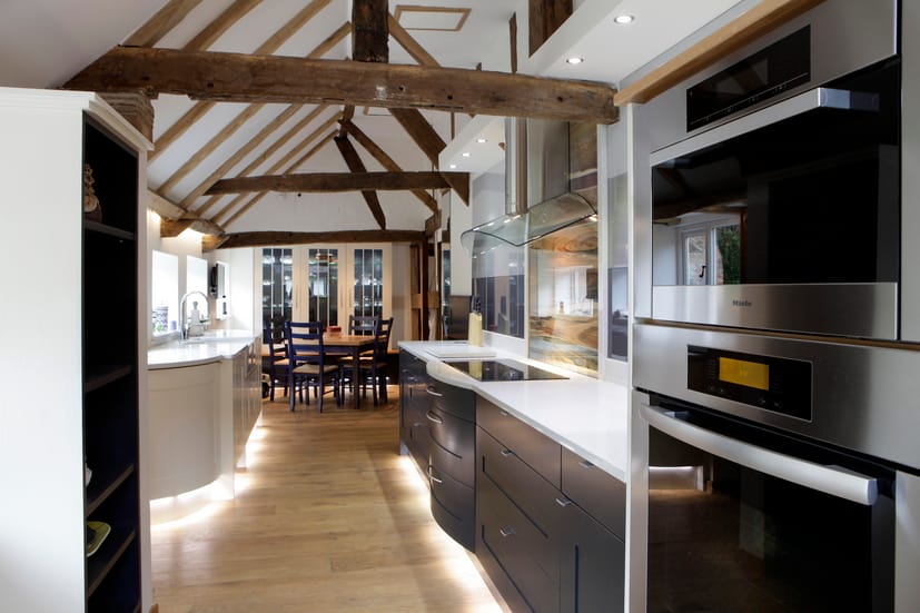 A modern galley-style kitchen set within a vaulted open-plan space with oak beams