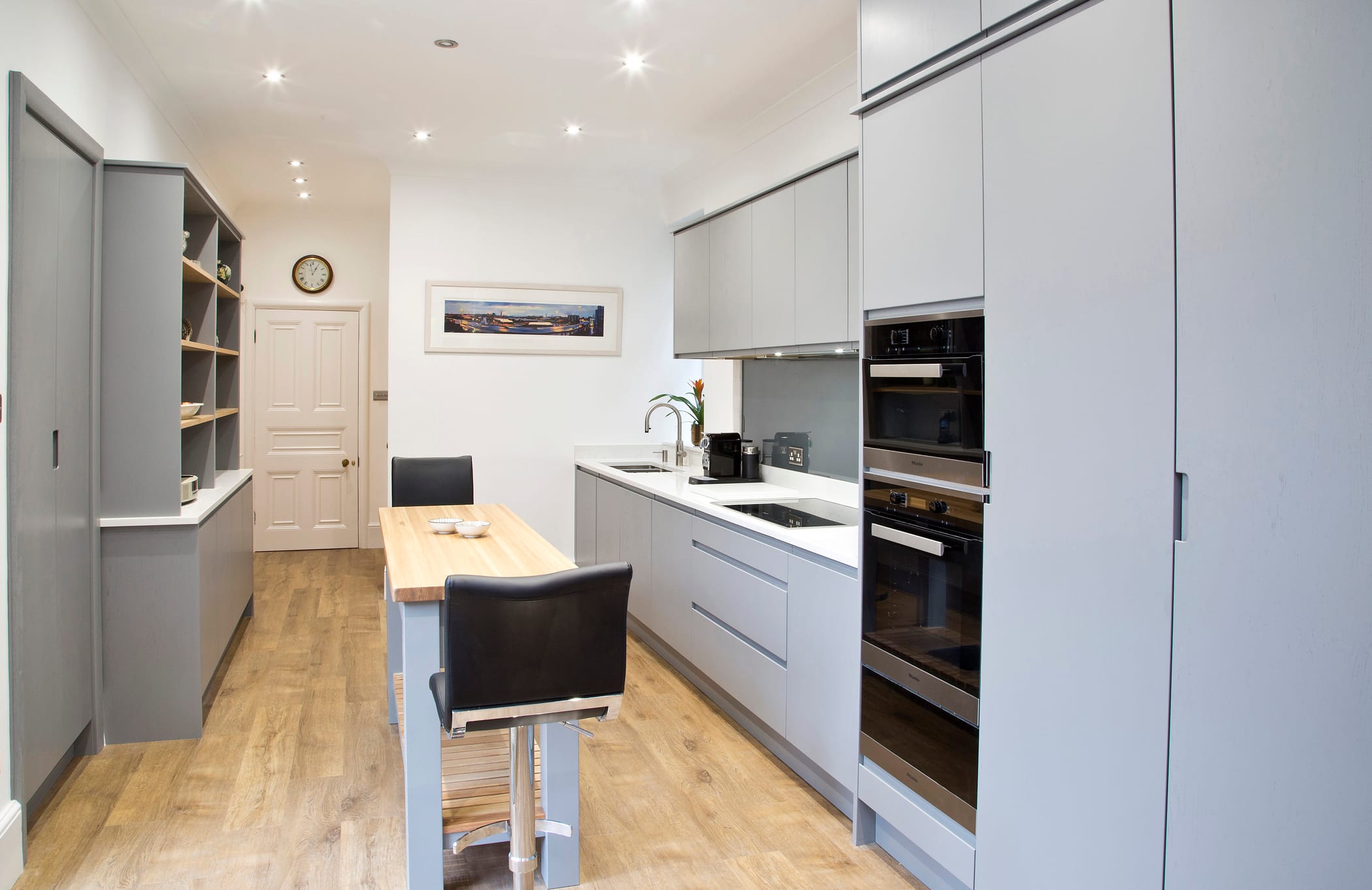 A galley kitchen with pale grey flat panel doors and a mixture of full height and split-level cabinetry plus a shelving unit and simple breakfast bar