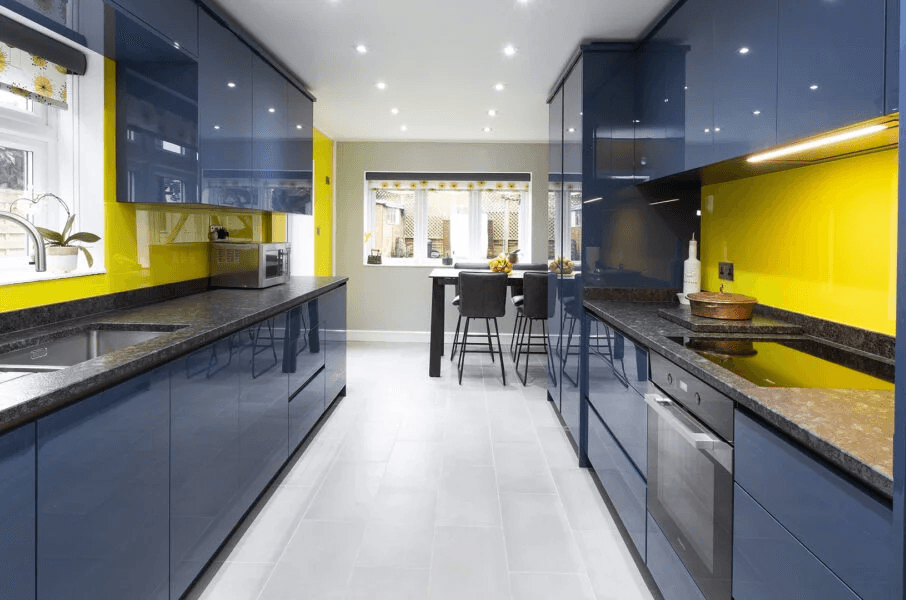 A modern blue and sunshine yellow galley kitchen with gloss acrylic cabinetry and grey granite countertops.