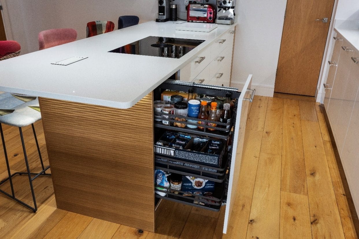 A galley kitchen with an innovative pull-out larder set within a stylish, quartz topped kitchen island featuring decorative panelling and a BORA hob.
