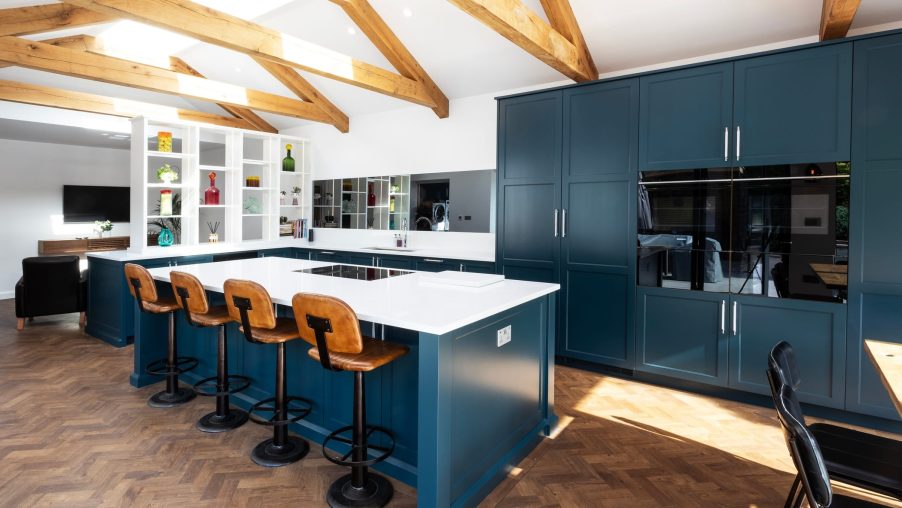 A rich blue painted modern shaker kitchen with vaulted oak beams and simple white paintwork and countertops.