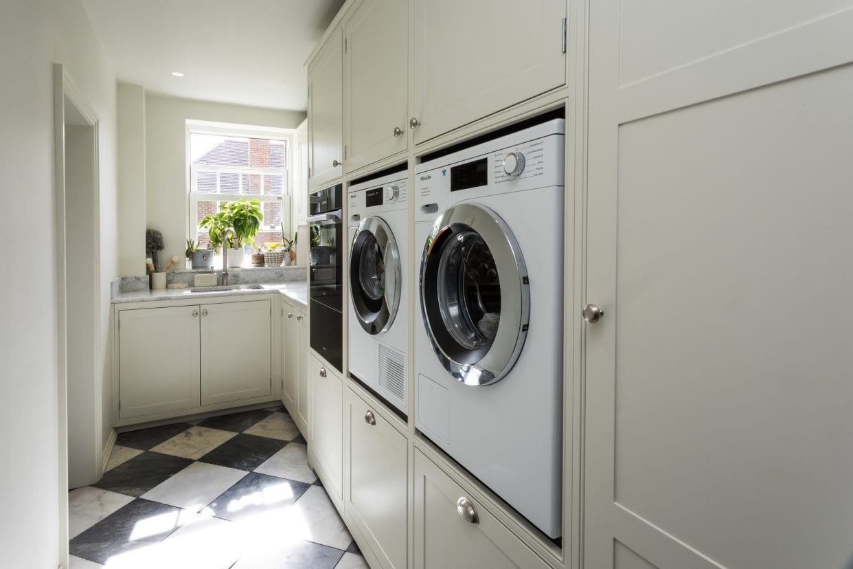 A bright utility space with eye-level laundry appliances and a sink under the window.