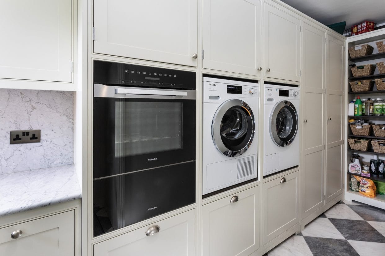 A bright utility space with eye-level laundry appliances, oven and a wall of larder storage.
