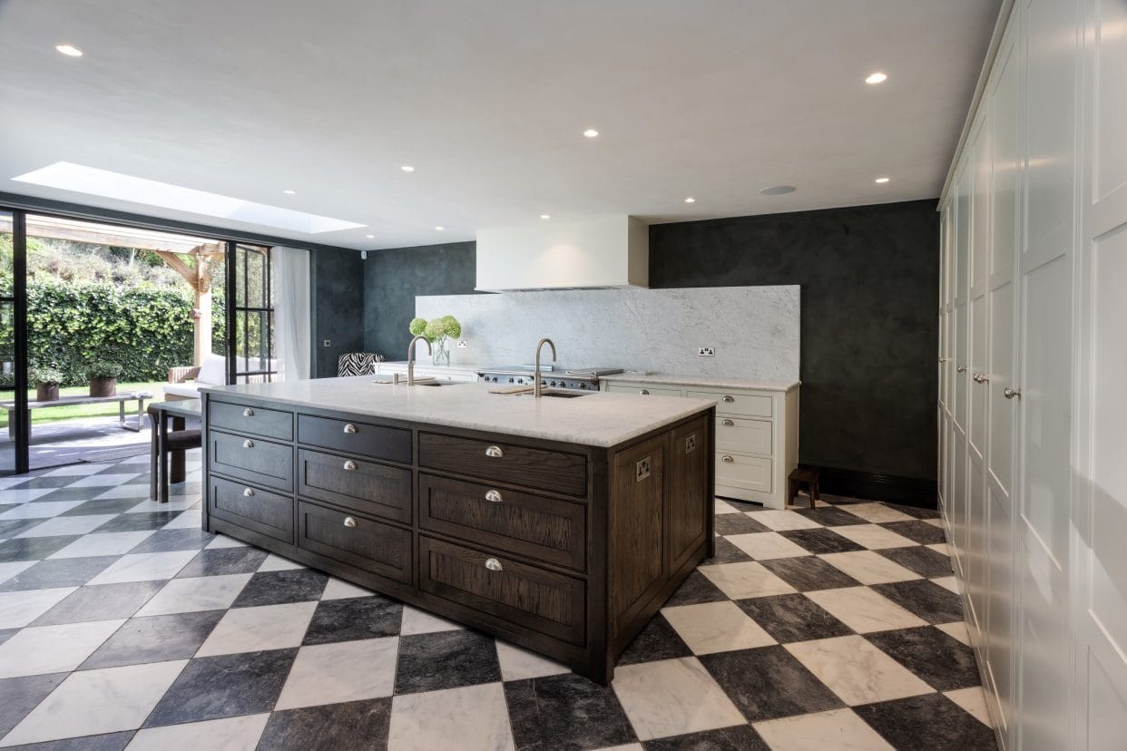 A striking modern shaker kitchen island in deep rich wood tones with marble countertop, there are black and white Revival-style floor tiles and a wall of floor to ceiling shaker cabinets to the right.