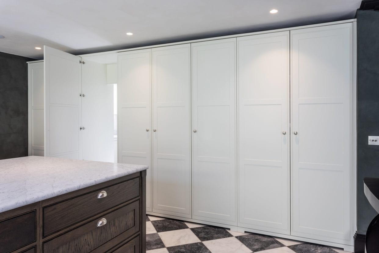 A wall of floor to ceiling shaker cabinetry with an open door to a lit room.