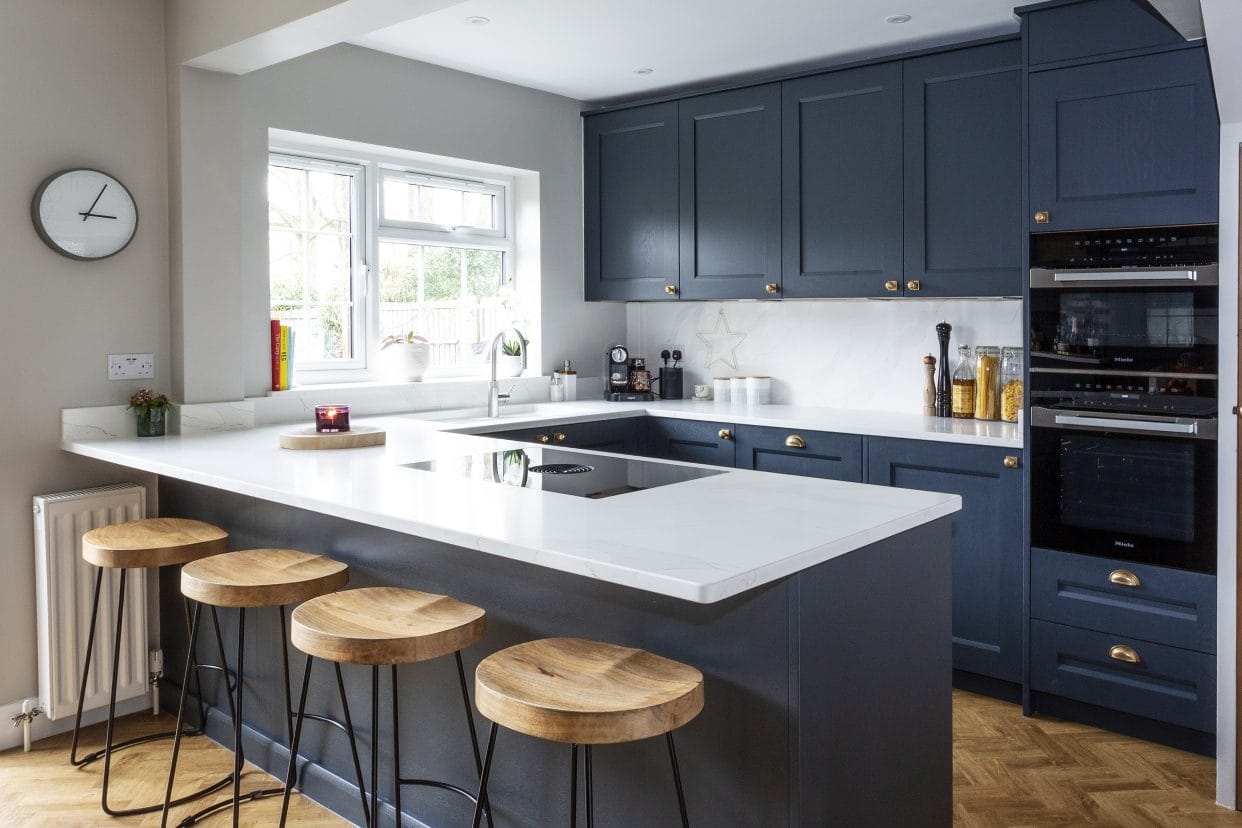 A U-shaped kitchen with deep blue handmade shaker cabinetry and brass handles.