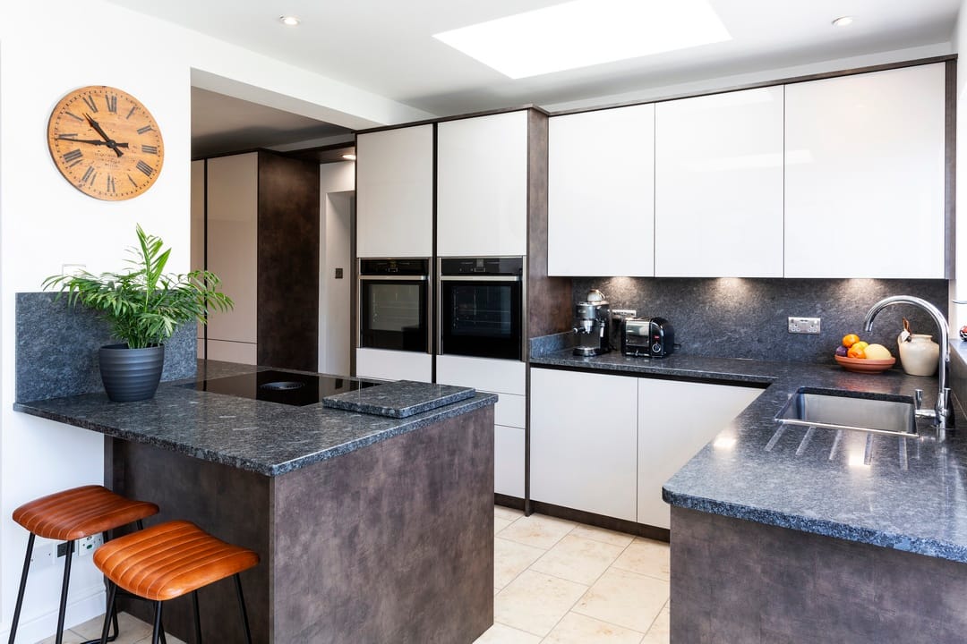 A modern L-shaped kitchen with white flat panel cabinetry contrasting with rich grey granite worktops. There is space for an island breakfast bar.