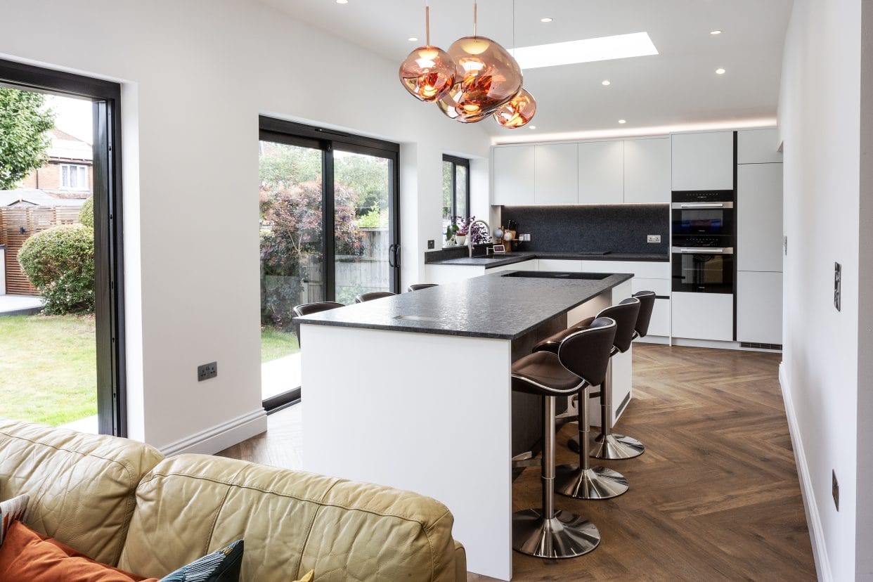 An understated L-shaped kitchen in black and white with statement copper pendant lights above the central island.