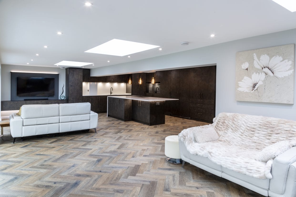 A very spacious kitchen/living room with an L-shaped kitchen at one end with split level and full height cabinetry and a large island separating the kitchen and living areas.