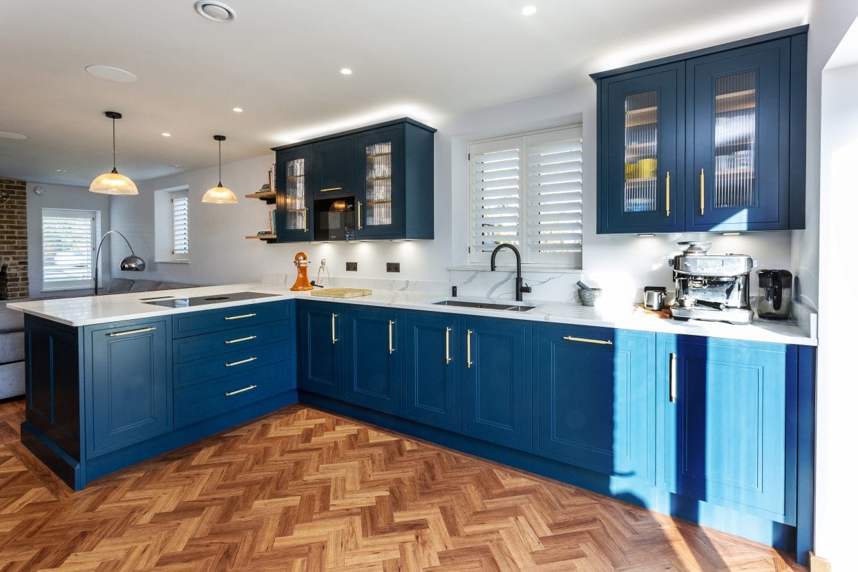 A modern, L-shaped shaker kitchen painted in a rich teal blue with brass bar handles.